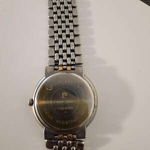 May include: A stainless steel Pierre Cardin watch with a silver band and a round watch face. The back of the watch is visible, displaying the brand name, model number P46-8084, and "Water Resistant 3ATM".