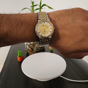 May include: A gold and silver Pierre Cardin wristwatch with a round face and a two-tone metal band. The watch is on a wrist. The watch face has gold accents and black hands. The watch is on a wrist.