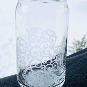 May include: A clear glass can with a white etched design of a stylized four-leaf clover.