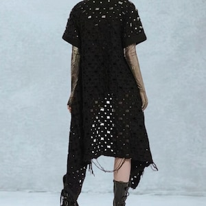 May include: Black, short-sleeved dress with a unique, openwork design. The dress features a high-low hemline and a textured appearance. The sleeves are short, and the dress has a slightly asymmetrical cut. The overall style is edgy and modern.