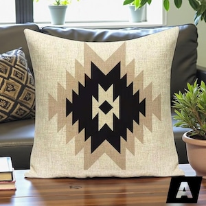 May include: Square decorative pillow with a geometric pattern in black, tan, and beige. The pillow has a textured appearance and is placed on a dark brown surface. The design is centered on the pillow.