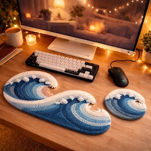 Pode incluir: Uma configuração de mesa de crochê com um mousepad e um porta-copos em forma de onda em tons de azul e branco. Um teclado preto e branco e um mouse preto estão em uma mesa de madeira. Um monitor de computador e uma caneca estão no fundo.