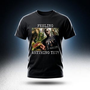 Op de afbeelding: Zwart t-shirt met een afbeelding van een persoon en een Venus vliegenvanger. Het shirt heeft de tekst "FEELING ANYTHING YET?" boven en onder de afbeelding. De afbeelding op het shirt in het shirt zegt "LOGGED OUT OF REALITY".