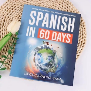 May include: A book titled "Spanish in 60 Days" with a blue cover. The cover features the text "Spanish in 60 Days" in large white and orange letters. The book's cover also includes an illustration of the Earth with buildings and airplanes.