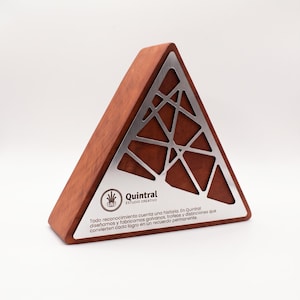 May include: A triangular award plaque made of reddish-brown wood featuring a silver metal overlay with a geometric lattice pattern. The metal plate includes the logo for Quintral Estudio Creativo and Spanish text about creating lasting memories.