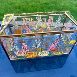 May include: A rectangular glass card box with a gold metal frame, featuring hand-painted floral designs in shades of pink, yellow, and blue. The top glass panel displays the gold-colored text "THE" and a cursive script "Days".