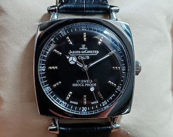 May include: A Jaeger-LeCoultre Club wristwatch with a square silver-tone case and a black dial. The dial features silver-tone hands, hour markers, and the text JAEGER-LECOULTRE CLUB, 17 JEWELS, SHOCK PROOF, and SWISS MADE. It has a black leather strap.