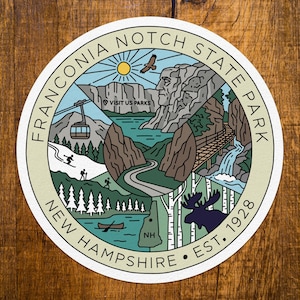 May include: A circular sticker featuring a graphic illustration of Franconia Notch State Park in New Hampshire. The design includes a mountain landscape, a cable car, a waterfall, a moose, a canoe, and the text Franconia Notch State Park New Hampshire Est. 1928.