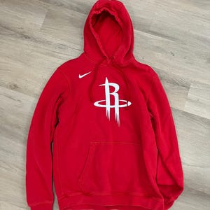 Puede incluir: Sudadera con capucha roja con el logotipo blanco de los Houston Rockets en la parte delantera. Cuenta con una capucha con cordones, un bolsillo delantero y un peque&ntilde;o logotipo blanco de Nike. La sudadera est&aacute; hecha de un material suave.