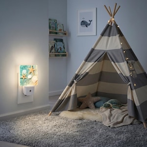May include: A square plug-in night light featuring a printed design of two tan starfish and two white seashells on a light blue water background. The light is illuminated and plugged into a white wall outlet next to a gray and white striped teepee.
