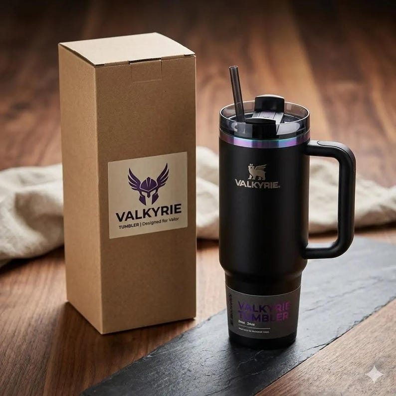 May include: A matte black stainless steel tumbler with a handle, a clear lid, and a straw. The tumbler features the Valkyrie logo and text. It is accompanied by a tall, rectangular cardboard box with a Valkyrie logo sticker on the front side.