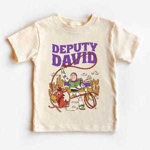 Personalized Sheriff Shirt, Custom Deputy Name T-Shirt, Space Ranger Cowboy Tee, Kids Western Birthday Gift, Toddler Buzz Lightyear Shirt

Step into an adventure-filled world for your little hero! This custom-designed t-shirt blends a beloved space-themed character with a fun western twist, sparking your child's imagination. It is the perfect outfit for birthday parties and a stylish choice for everyday playtime.