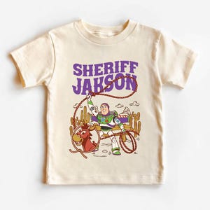 Personalized Sheriff Shirt, Custom Deputy Name T-Shirt, Space Ranger Cowboy Tee, Kids Western Birthday Gift, Toddler Buzz Lightyear Shirt

Step into an adventure-filled world for your little hero! This custom-designed t-shirt blends a beloved space-themed character with a fun western twist, sparking your child's imagination. It is the perfect outfit for birthday parties and a stylish choice for everyday playtime.