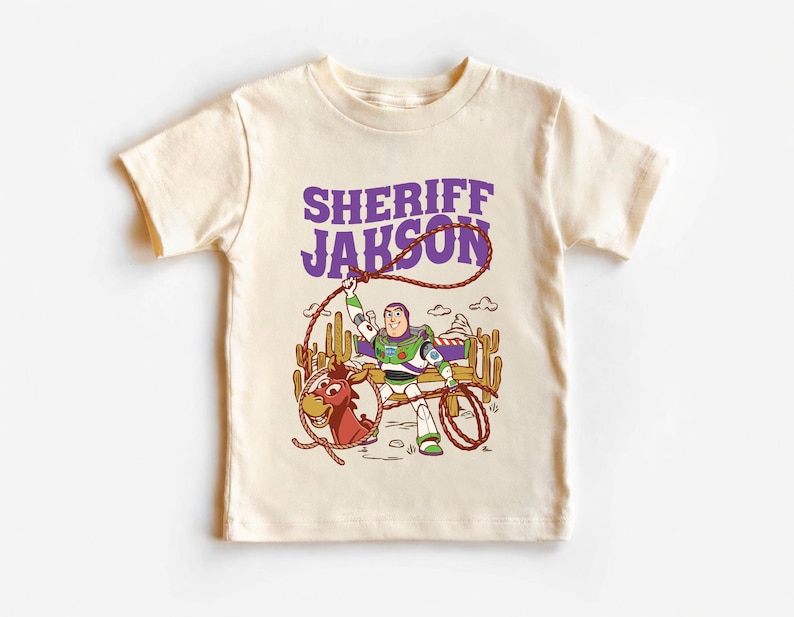 Personalized Sheriff Shirt, Custom Deputy Name T-Shirt, Space Ranger Cowboy Tee, Kids Western Birthday Gift, Toddler Buzz Lightyear Shirt

Step into an adventure-filled world for your little hero! This custom-designed t-shirt blends a beloved space-themed character with a fun western twist, sparking your child's imagination. It is the perfect outfit for birthday parties and a stylish choice for everyday playtime.