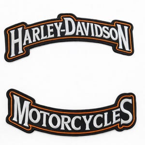 May include: Two black and white Harley-Davidson patches. The top patch reads "HARLEY-DAVIDSON" in white, arched text with an orange border. The bottom patch reads "MOTORCYCLES" in white, arched text with an orange border.
