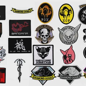 Puede incluir: Una colección de parches bordados con varios diseños. Incluye parches con textos como "STEALTH", "BANDANA", "OUTER HEAVEN" y "DIAMOND DOGS". Los parches presentan imágenes de un zorro, una calavera y otros símbolos.