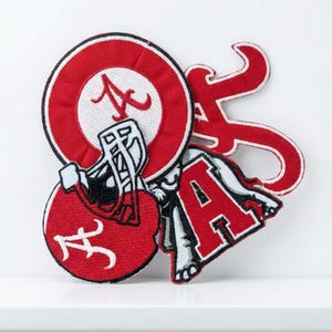 May include: A collection of red and white embroidered patches featuring the letter "A" and a football helmet. One patch is a circular design with the letter "A" in the center. Another patch is the letter "A" in a script font.