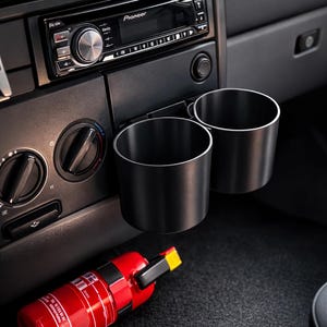 Peut inclure: Intérieur de voiture avec un autoradio Pioneer, deux porte-gobelets noirs et un extincteur rouge. Le tableau de bord est noir. L'image est bien éclairée.