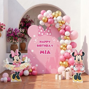 Puede incluir: Decoraci&oacute;n de fiesta de cumplea&ntilde;os con tem&aacute;tica de Minnie Mouse. Cuenta con un gran tel&oacute;n de fondo rosa con una silueta de Minnie, el texto "Happy Birthday Mia" y un dise&ntilde;o de castillo. Globos rosas, blancos y dorados, junto con recortes de Minnie Mouse y cajas de regalo completan la escena festiva.