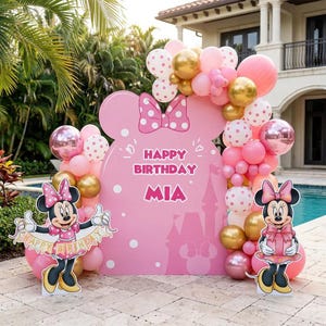 Puede incluir: Decoraci&oacute;n de fiesta de cumplea&ntilde;os con tem&aacute;tica de Minnie Mouse. Cuenta con un gran recorte rosa con forma de cabeza de Minnie con el texto "Happy Birthday Mia". Globos rosas, dorados y blancos rodean el recorte y recortes de Minnie Mouse.