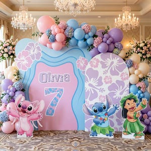 May include: A birthday party backdrop featuring a pink and blue design with the name "Olivia" and the number "7". The backdrop is decorated with balloons, floral arrangements, and cutouts of characters from the movie Lilo & Stitch.