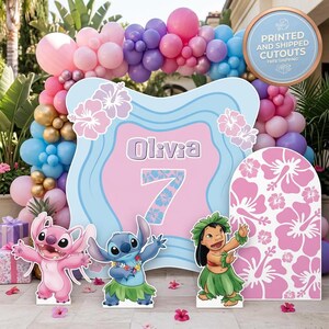 May include: A party decoration set featuring a large sign with the name "Olivia" and the number "7", along with cutouts of cartoon characters and a floral arch made of balloons in pink, blue, purple, and gold. The sign also has hibiscus flowers.