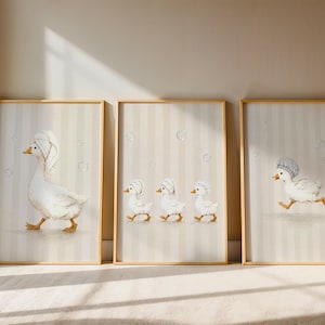 May include: Three framed wall art prints featuring white ducks with orange beaks and feet. The left print shows a large duck with a towel on its head. The centre print shows three small ducklings with towels. The right print shows a duckling with a shower cap.