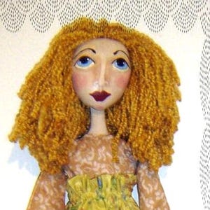 May include: A handcrafted fabric doll featuring curly golden-yellow yarn hair, painted facial features with blue eyes and dark lips, and a long-sleeved top with a light brown patterned fabric paired with a yellow skirt featuring a floral print.
