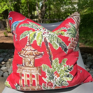 May include: Red throw pillow with a tropical print featuring palm trees, pagodas, and birds. The pillow is made of a soft, linen-like fabric.