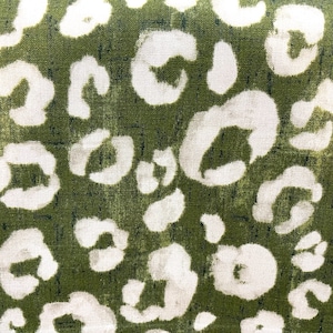 May include: Green fabric with a white leopard print pattern. The fabric has a textured surface.