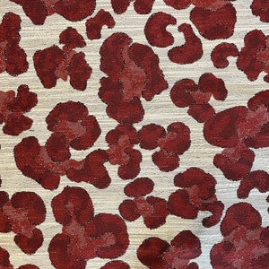 May include: A close-up of a fabric with a white background and a repeating pattern of maroon-colored leopard spots.