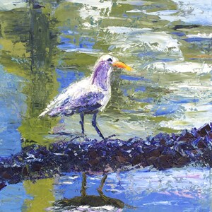 May include: A white bird with a yellow beak stands on a log in a blue and green water scene. The bird's reflection is visible in the water.