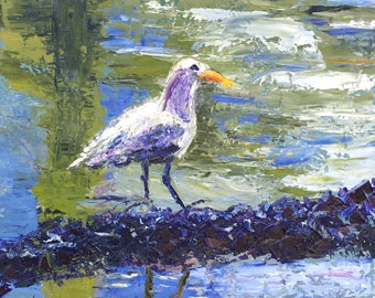 Puede incluir: Un pájaro blanco con un pico amarillo se posa sobre un tronco en una escena de agua azul y verde. El reflejo del pájaro es visible en el agua.