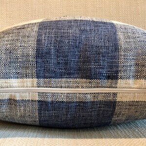 Puede incluir: Una almohada de tiro a cuadros azul y blanco con cierre de cremallera. La almohada est&aacute; hecha de una tela tejida con una textura sutil.