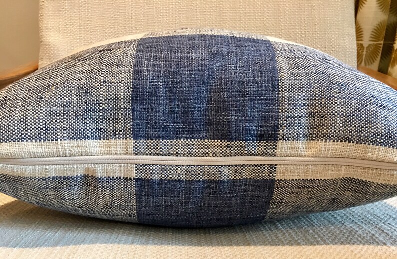 Puede incluir: Una almohada de tiro a cuadros azul y blanco con cierre de cremallera. La almohada est&aacute; hecha de una tela tejida con una textura sutil.