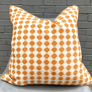 May include: A white and orange patterned throw pillow with a geometric design. The pillow is made of a soft, textured fabric.