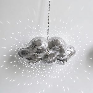 May include: A cloud-shaped disco ball hanging from a chain. The silver mirrored surface reflects light, creating a sparkling effect on the white background. The unique design adds a touch of whimsy to any space.