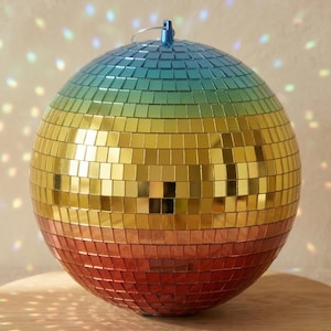 May include: A spherical disco ball with a colour gradient from blue to red. The surface is covered in small, square mirrored tiles. A small blue loop is at the top for hanging. The ball is designed to reflect light.