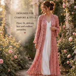 May include: A long, open-front duster cardigan in a dusty rose colour, featuring intricate floral lace patterns, long sleeves with flared cuffs, and a floor-length hem, worn over a simple white slip dress. Text reads: DESIGNED FOR COMFORT & STYLE.