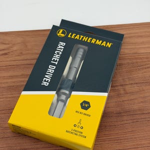 May include: A Leatherman ratchet driver in its original packaging. The box is black and yellow, with the Leatherman logo and the words "RATCHET DRIVER" printed on it. The box also indicates it is a 1/4" hex bit driver with a 3-position ratcheting system.