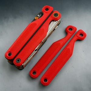 May include: A folded red multi-tool with a textured grip and black hardware, featuring a blade marked MagnaCut. Beside the tool are two separate red handle components, each with a circular hole at the top and bottom, matching the tool's design.