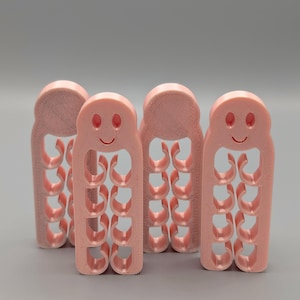 May include: Four light pink, 3D-printed cable organizers standing upright. Each organizer features a rounded top with a simple smiley face design and a vertical column of four circular cutouts designed to hold and manage individual electrical cords.