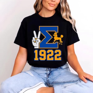 May include: Black t-shirt with a blue and gold graphic. The graphic includes a peace sign, the Greek letter Sigma, a poodle on roller skates, and the number 1922. The shirt is a casual style.
