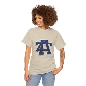 Könnte beinhalten: Beiges T-Shirt mit einem marineblauen und weißen Buchstaben "A"-Design. Der Buchstabe ist ein Aufnäher im College-Stil. Das Shirt ist ein lässiges Oberteil mit kurzen Ärmeln.
