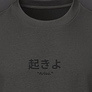 May include: Dark gray t-shirt with short sleeves and a crew neck. The shirt features Japanese characters and the English word "Arise." printed in a darker shade of gray. The shirt has a relaxed fit.