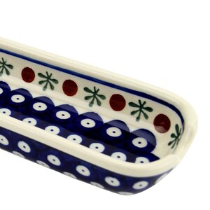 May include: A rectangular ceramic serving dish with a blue and white floral pattern. The dish has a scalloped edge with a dark blue border and is decorated with white dots, red circles, and green star-like shapes. The dish has a small handle on one end.