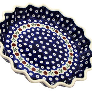 May include: Oval-shaped ceramic serving dish with a dark blue background and white polka dots. The rim is scalloped and white. The dish features a decorative pattern of white dots, brown circles, and green star-like shapes.