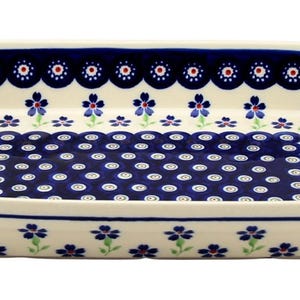 May include: Rectangular ceramic serving dish with a cream-colored base and a blue floral pattern. The rim features a scalloped edge with alternating blue and red accents. The interior has a central blue design with white dots.