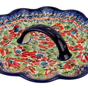 May include: A ceramic serving platter with a scalloped edge and a dark blue handle. The platter features a floral pattern with red flowers, green leaves, and blue accents. The rim is dark blue with a decorative border.