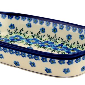 May include: A ceramic rectangular baking dish with a blue floral pattern. The dish has a cream-colored base with blue flowers and green leaves. The rim and handles are a deep blue. The dish is designed for baking and serving.